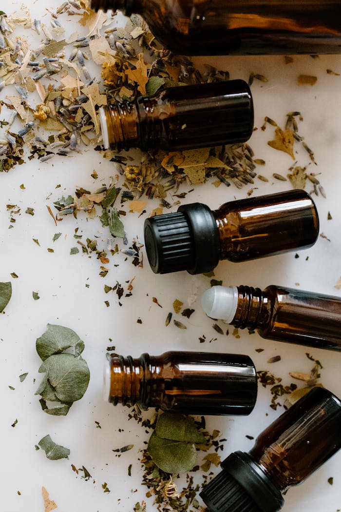 Flat lay of amber glass bottles and dried herbs for aromatherapy on a white surface.
