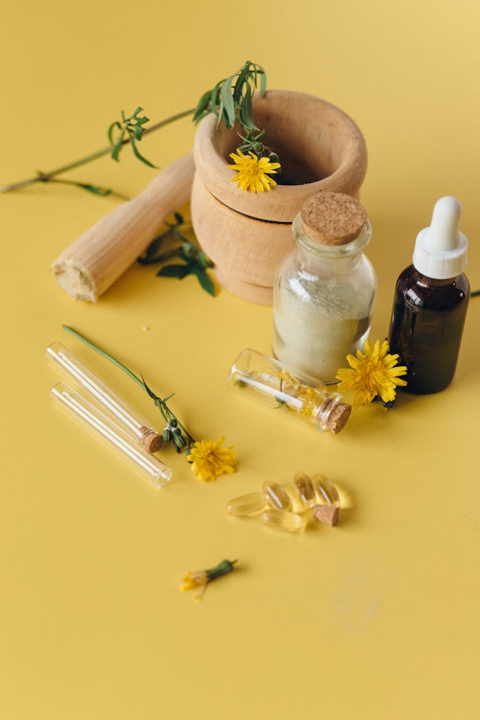 Collection of herbal ingredients with test tubes and glass bottles on a yellow surface.